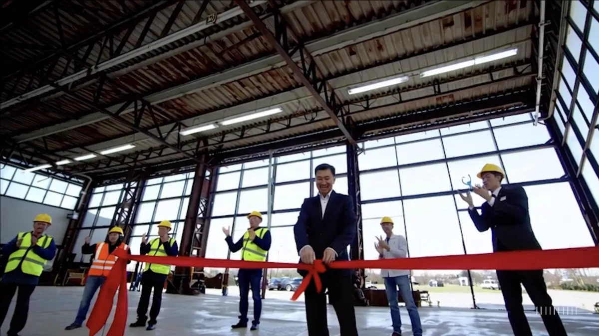 An AI-generated video of a factory floor with glass walls and a man in a black suit holding a floating red ribbon.