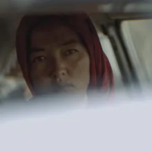 A young woman wearing a red headscarf gazes at the camera.